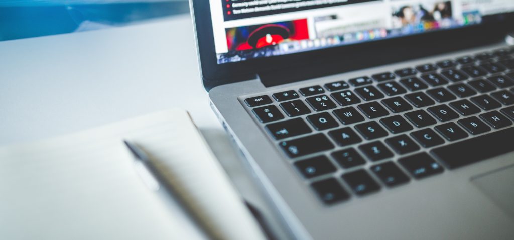 Wykadrowane zdjęcie przedstawiające część leżącego na biurku laptopa oraz notesu